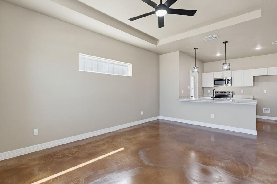 Unfurnished living room with finished concrete floors, a tray ceiling, ceiling fan, and recessed lighting