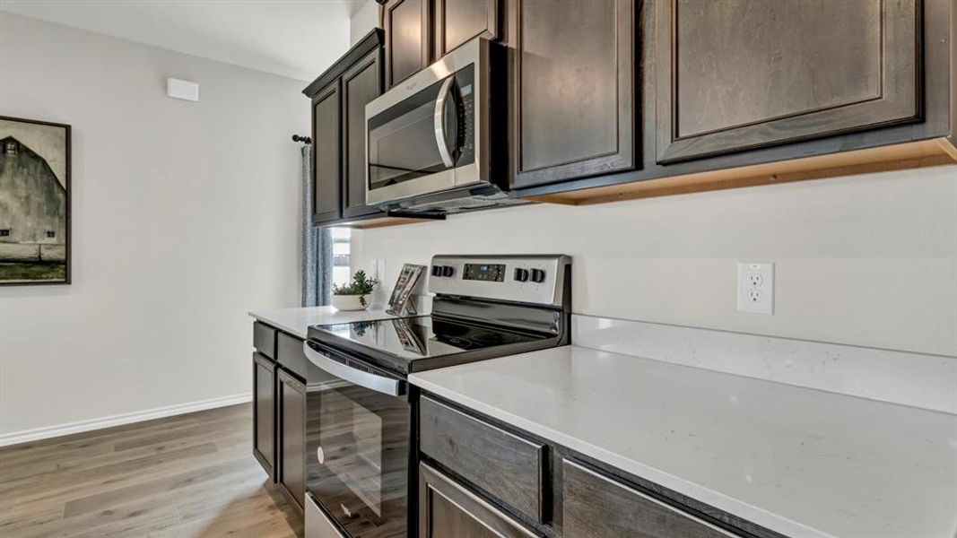 Modern kitchen featuring dark wood-finish cabinetry, light stone countertops, stainless steel microwave, and a black electric range with a glass cooktop Modern kitchen featuring dark wood-finish cabinetry, light stone countertops, stainless steel microwave, and a black electric range with a glass cooktop