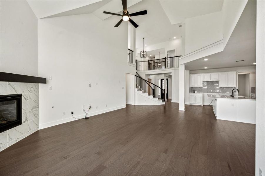 Unfurnished living room with a tiled fireplace, high vaulted ceiling, ceiling fan, and dark hardwood / wood-style floors