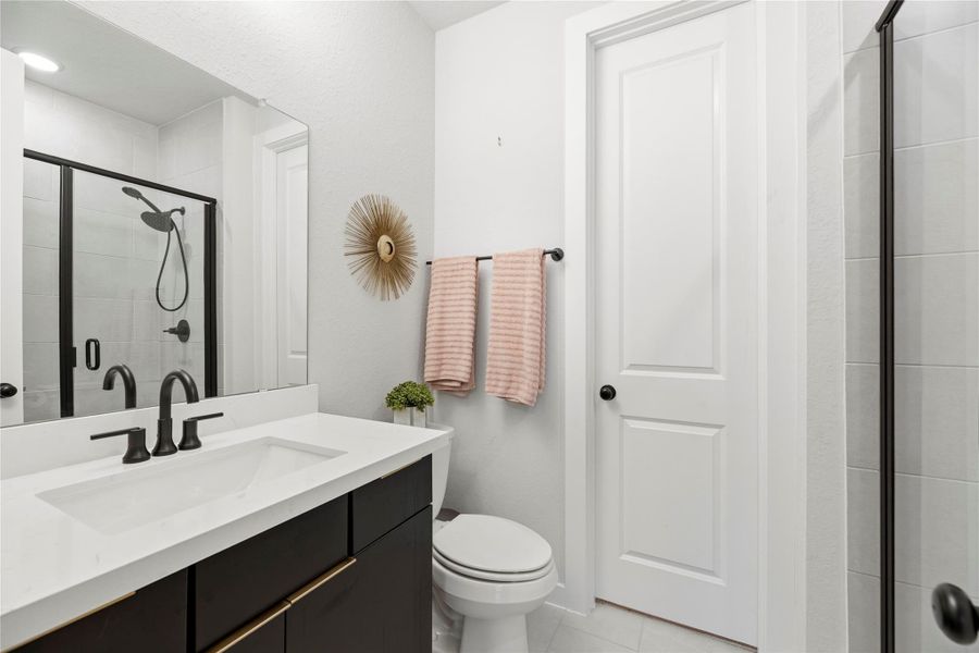 Modern private en suite bathroom with a sleek design featuring a black-framed glass shower, white countertop and dark cabinetry.
