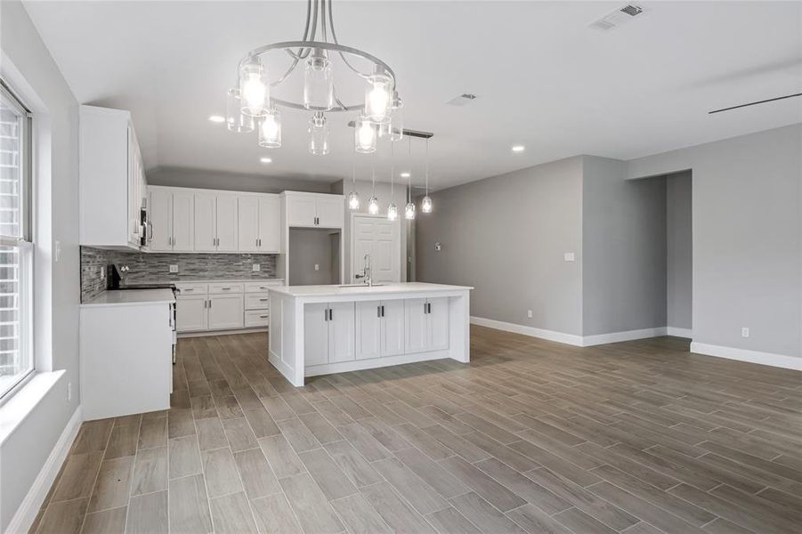 Kitchen featuring hanging light fixtures, white cabinets, decorative backsplash, sink, and a center island with sink