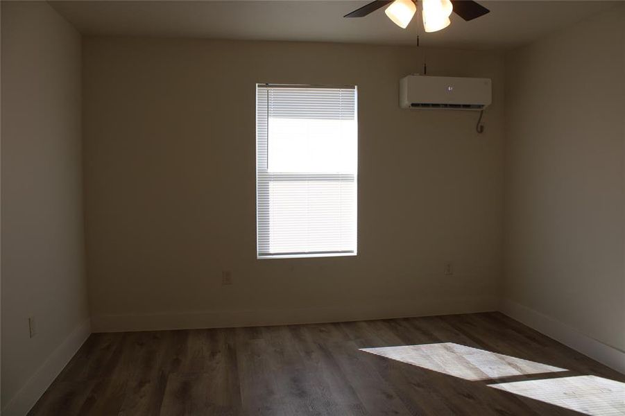 Spare room featuring dark wood finished floors, a wall mounted AC, and a ceiling fan