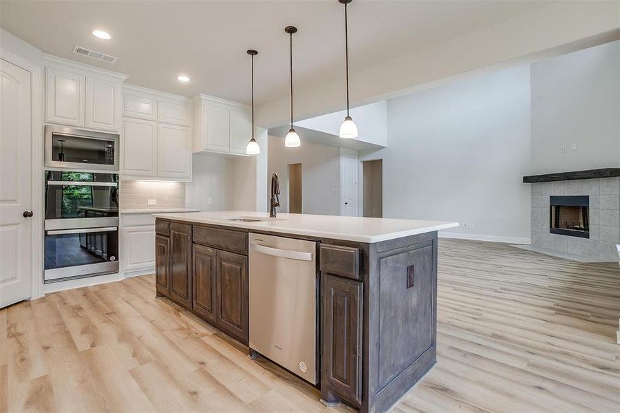 Kitchen featuring a tiled fireplace, light wood-type flooring, stainless steel appliances, and white cabinetry