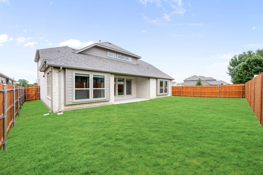 Backyard of a brick home with large green lawn, covered patio, and wood privacy fence