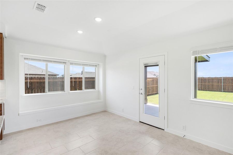 Bright empty room with tile floors, large windows, and glass back door leading to fenced yard