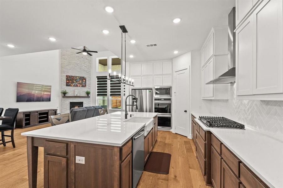 Kitchen featuring light wood-type flooring, open floor plan, decorative light fixtures, stainless exhaust hood, double convection ovens, and a professional grade gas cooktop