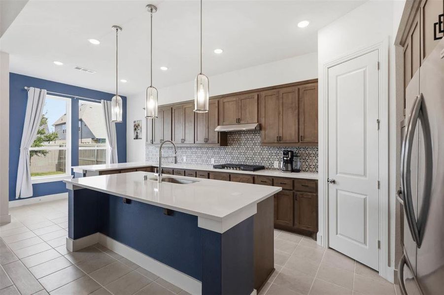 Contemporary kitchen featuring a large central island with a white countertop and blue-painted base, wood-finish cabinetry, a patterned tile backsplash, and recessed lighting