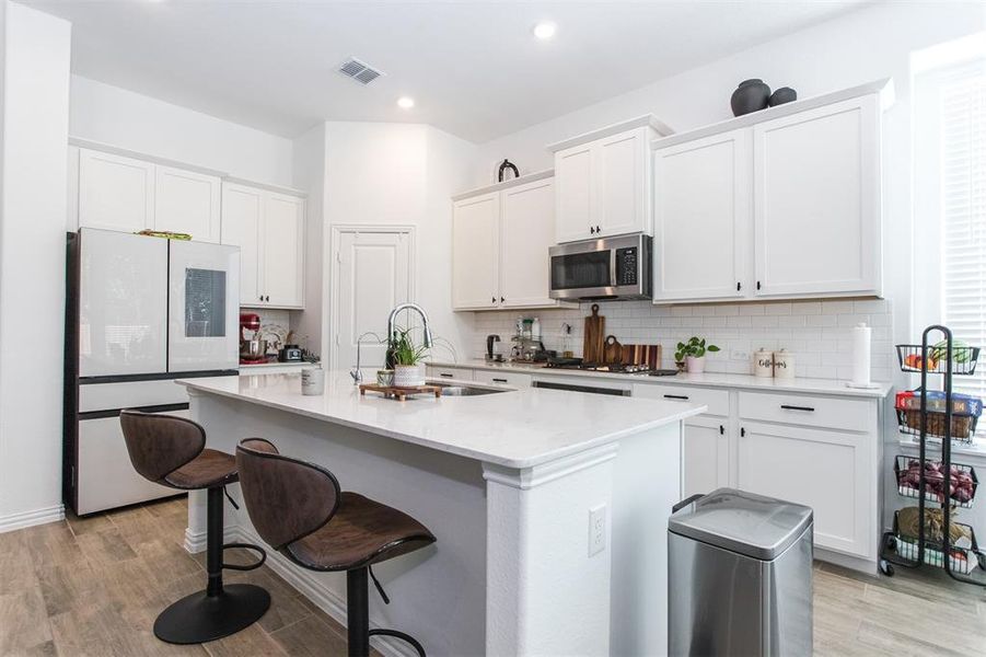 Kitchen featuring a kitchen island with sink, white refrigerator, sink, light hardwood / wood-style flooring, and white cabinetry