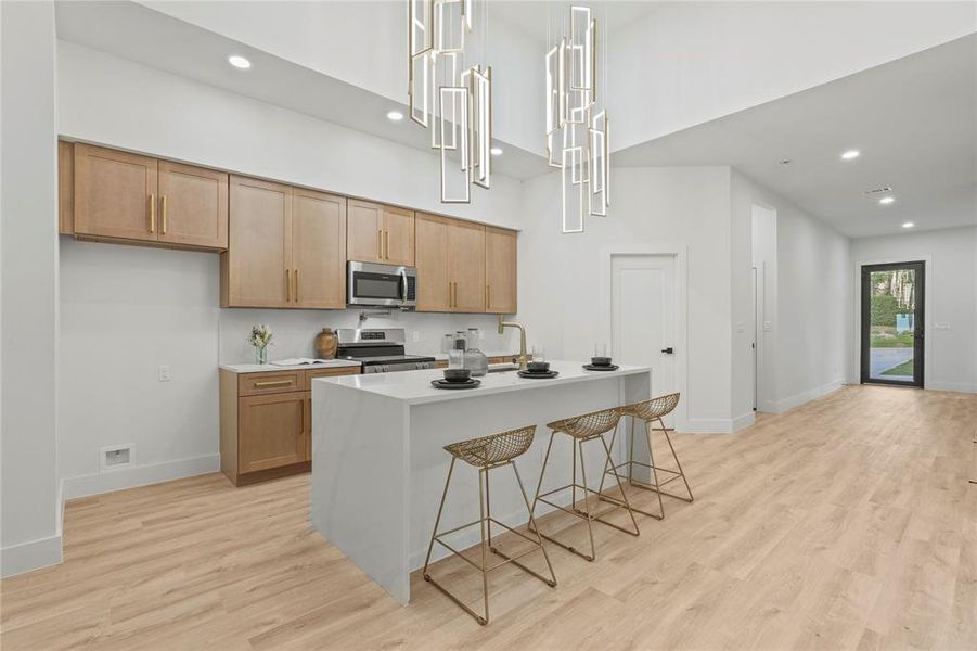 Kitchen featuring appliances with stainless steel finishes, a towering ceiling, recessed lighting, light wood finished floors, and baseboards Kitchen featuring appliances with stainless steel finishes, a towering ceiling, recessed lighting, light wood finished floors, and baseboards