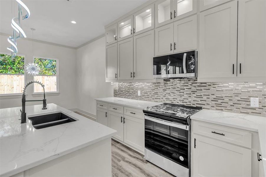 Kitchen featuring appliances with stainless steel finishes, white cabinetry, light stone countertops, tasteful backsplash, and hanging light fixtures