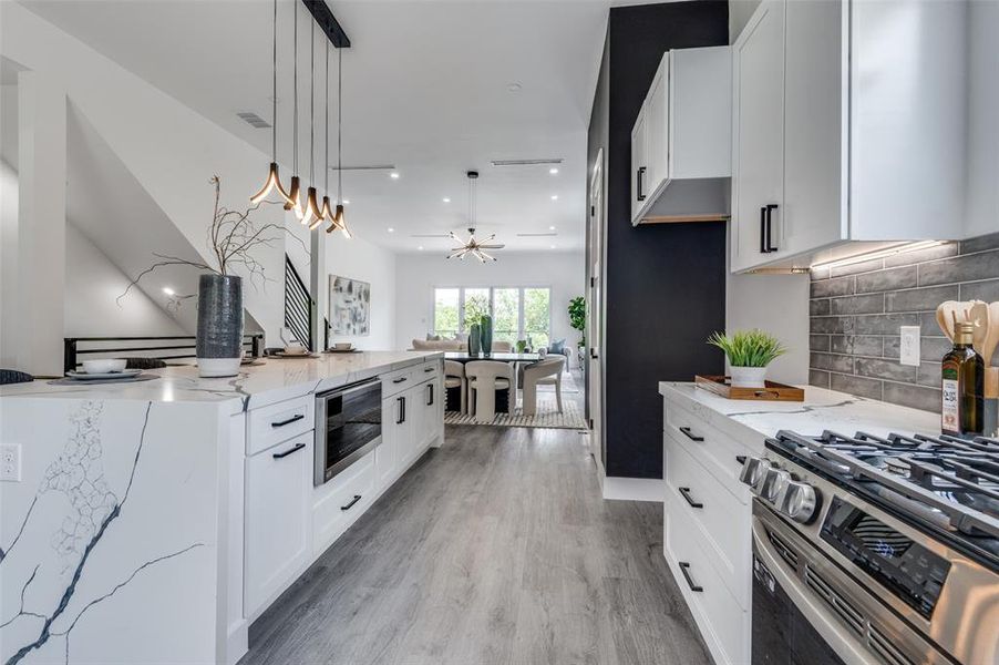 Kitchen with decorative backsplash, light hardwood / wood-style flooring, white cabinetry, light stone counters, and decorative light fixtures