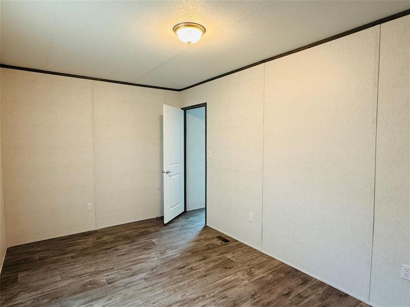 Spare room with dark wood-style flooring, a decorative wall, a textured ceiling, and crown molding