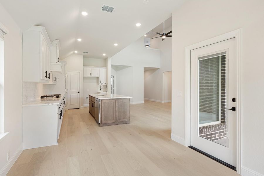 Open kitchen with white cabinets, center island, and light hardwood floors leading to living area Open kitchen with white cabinets, center island, and light hardwood floors leading to living area