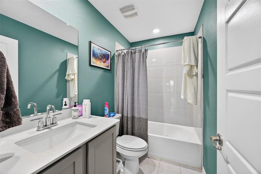 Bathroom featuring vanity, shower / bathtub combination with curtain, light tile patterned floors, and a textured wall