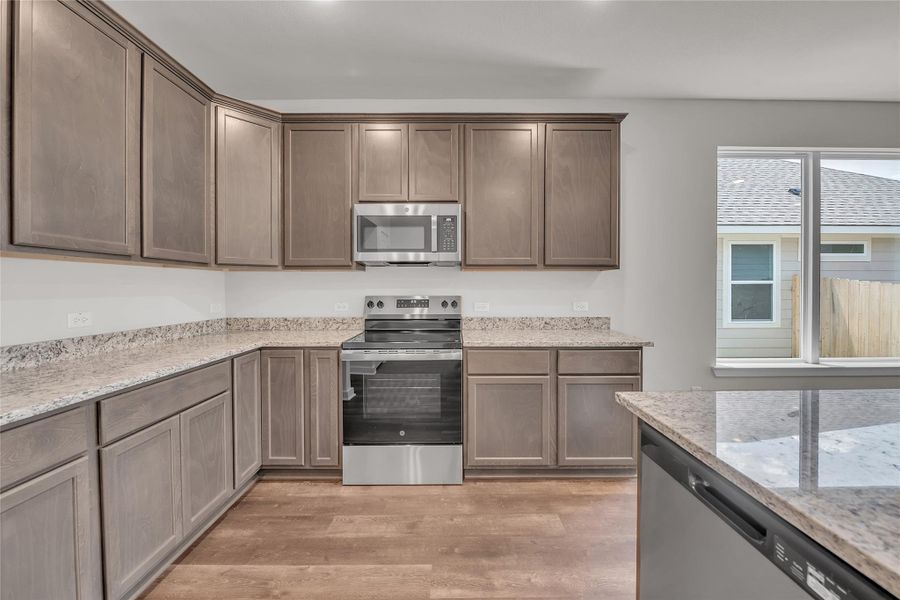 Kitchen featuring stainless steel appliances, light wood finished floors, light stone counters, and dark brown cabinetry Kitchen featuring stainless steel appliances, light wood finished floors, light stone counters, and dark brown cabinetry