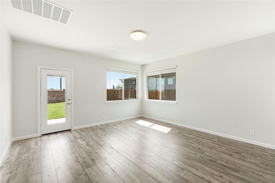 Empty room with light wood floors, white walls, two windows, and a back door to the yard