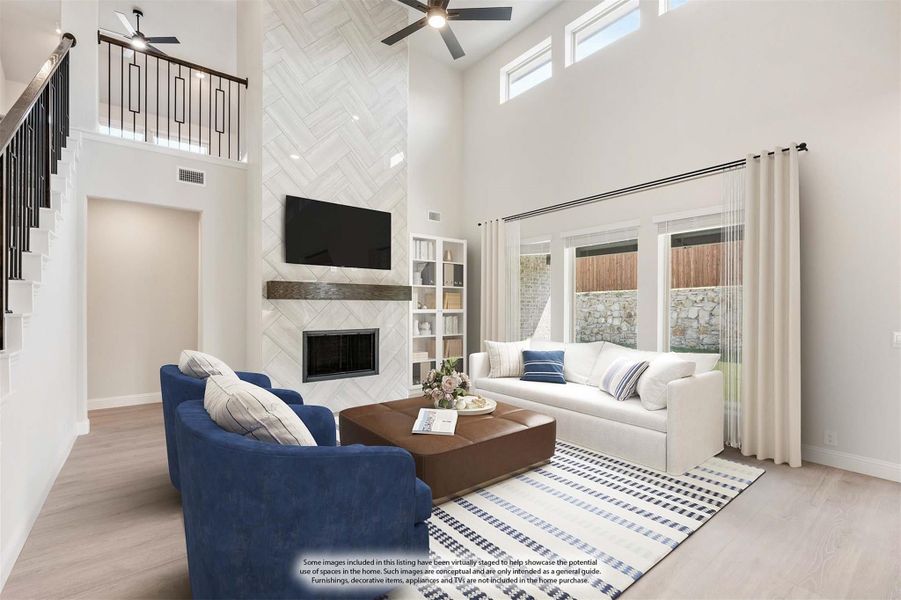 Living room with two-story ceiling, herringbone tile fireplace, ceiling fan, and blue accent chairs on light hardwood floors