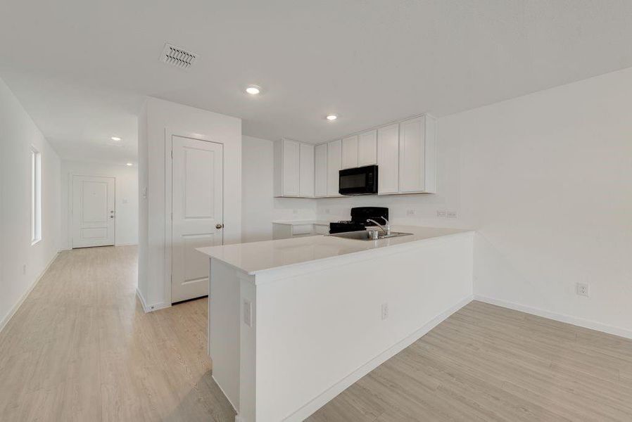 Kitchen featuring light wood-style flooring, white cabinetry, a peninsula, black microwave, and light countertops