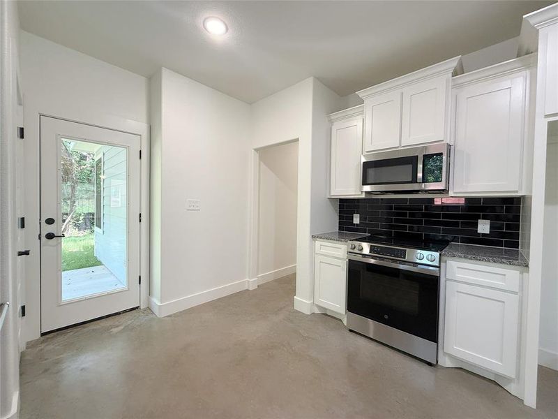 Kitchen with stainless steel appliances, backsplash, concrete floors, and white cabinetry