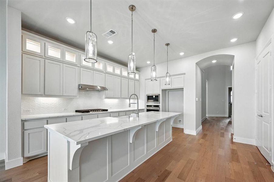 Kitchen featuring white cabinets, light wood-style floors, a breakfast bar area, light stone countertops, and decorative backsplash Kitchen featuring white cabinets, light wood-style floors, a breakfast bar area, light stone countertops, and decorative backsplash