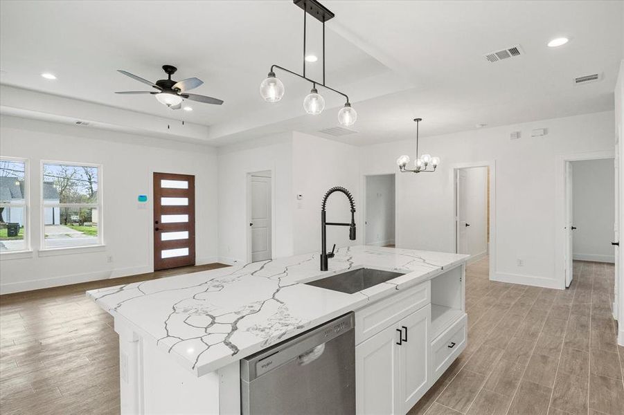 Kitchen featuring stainless steel dishwasher, a raised ceiling, a center island with sink, open floor plan, and white cabinetry