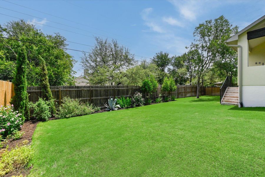 A spacious, verdant yard with mature landscaping and a well-maintained wooden fence.
