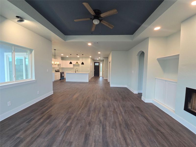Unfurnished living room with recessed lighting, ceiling fan, dark wood-type flooring, a tray ceiling, and arched walkways