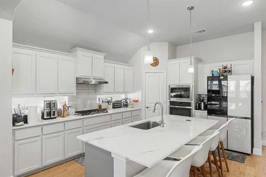 Modern kitchen featuring a large island with sink, white cabinetry, integrated stainless steel appliances, and a tile backsplash