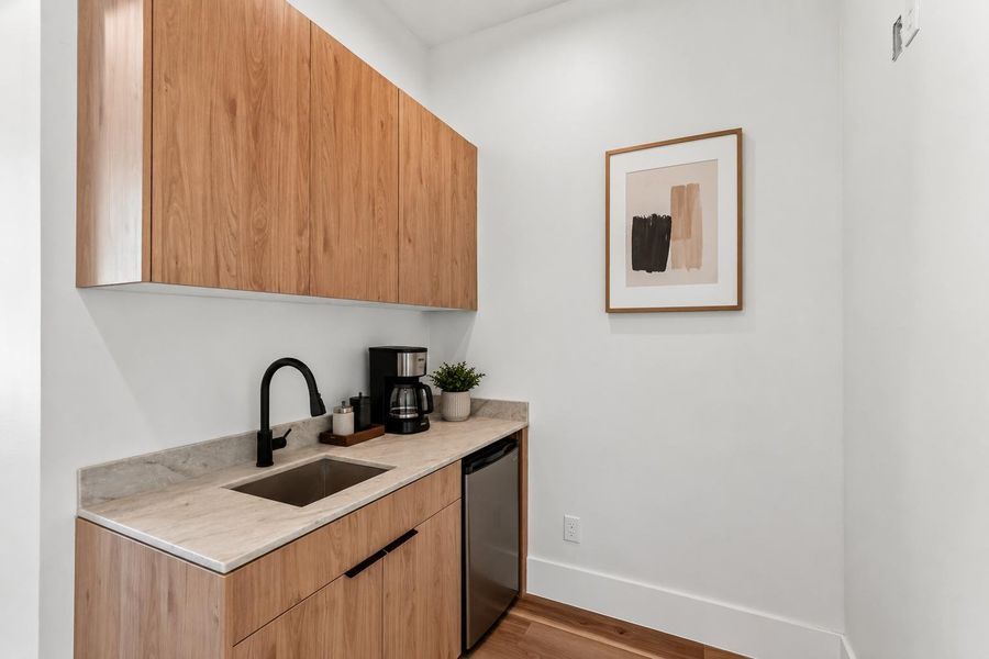 Functional guest kitchenette featuring a sink, upper and lower cabinet storage, and a dedicated space for a compact refrigerator.