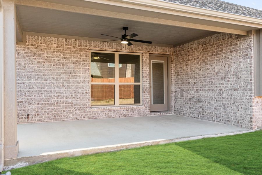 Covered back patio with ceiling fan, brick exterior, concrete floor, and back door entry overlooking green lawn Covered back patio with ceiling fan, brick exterior, concrete floor, and back door entry overlooking green lawn