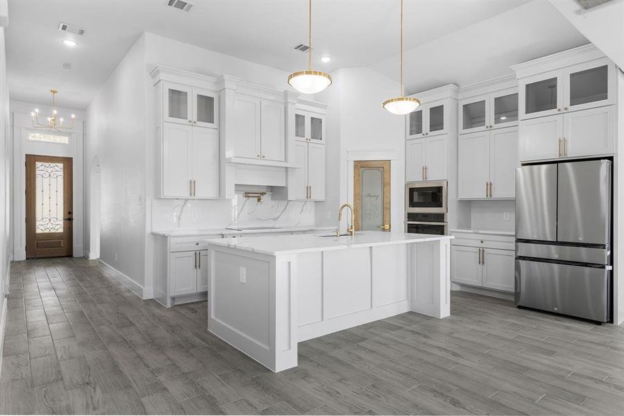 Kitchen with white cabinets, hanging light fixtures, an island with sink, appliances with stainless steel finishes, and light hardwood / wood-style floors