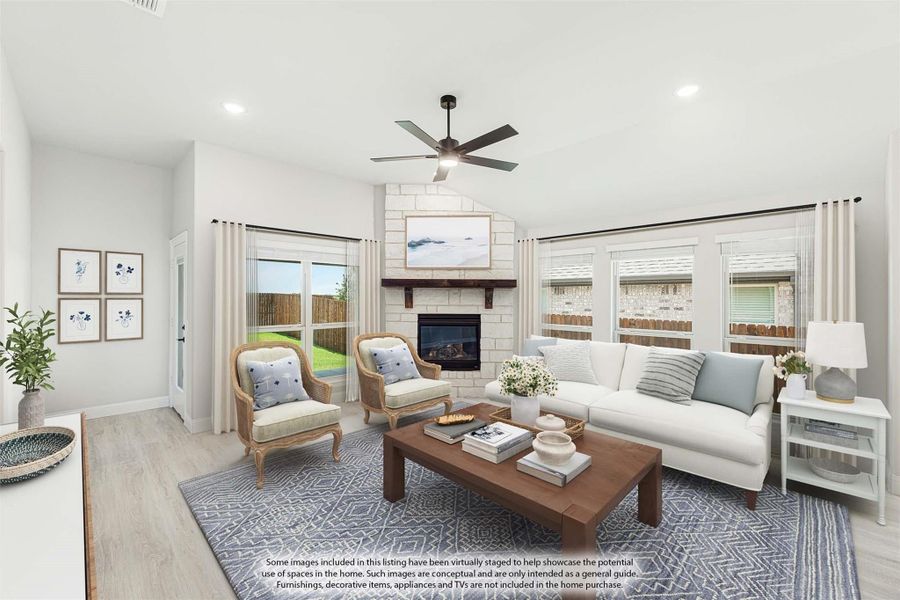 Living room with stone fireplace, ceiling fan, hardwood floors, and large windows with backyard view
