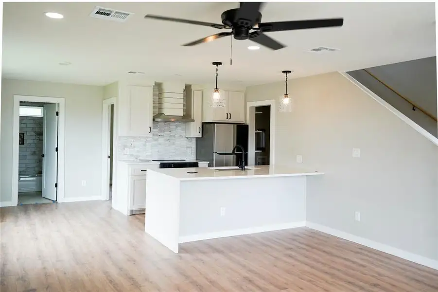 Kitchen with wall chimney range hood, freestanding refrigerator, tasteful backsplash, white cabinets, and recessed lighting