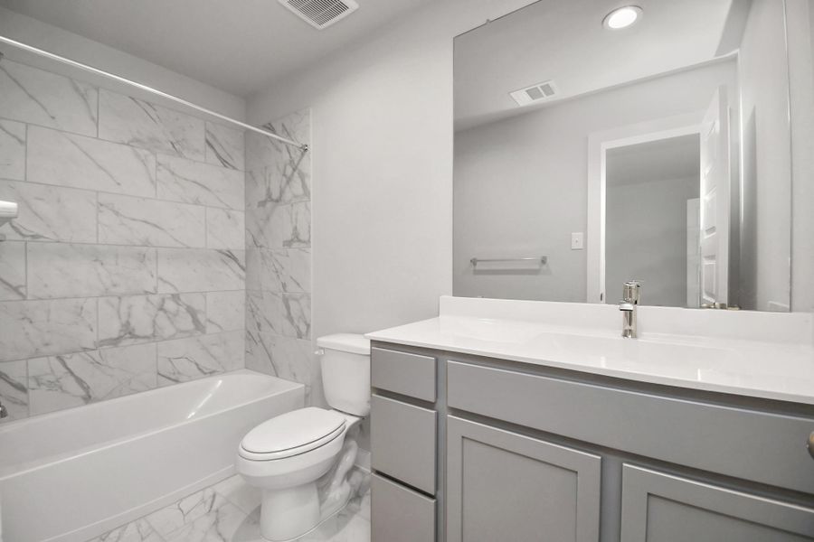 Experience sophistication in the secondary bathroom, where tile flooring complements a bath/shower combo with tile surround. Light wood cabinets enhance the space, while a distinctive barrel ceiling adds a touch of architectural elegance. Complete with a beautiful light countertop, this bathroom Sample photo of completed home with similar floor plan. As-built interior colors and selections may vary.
