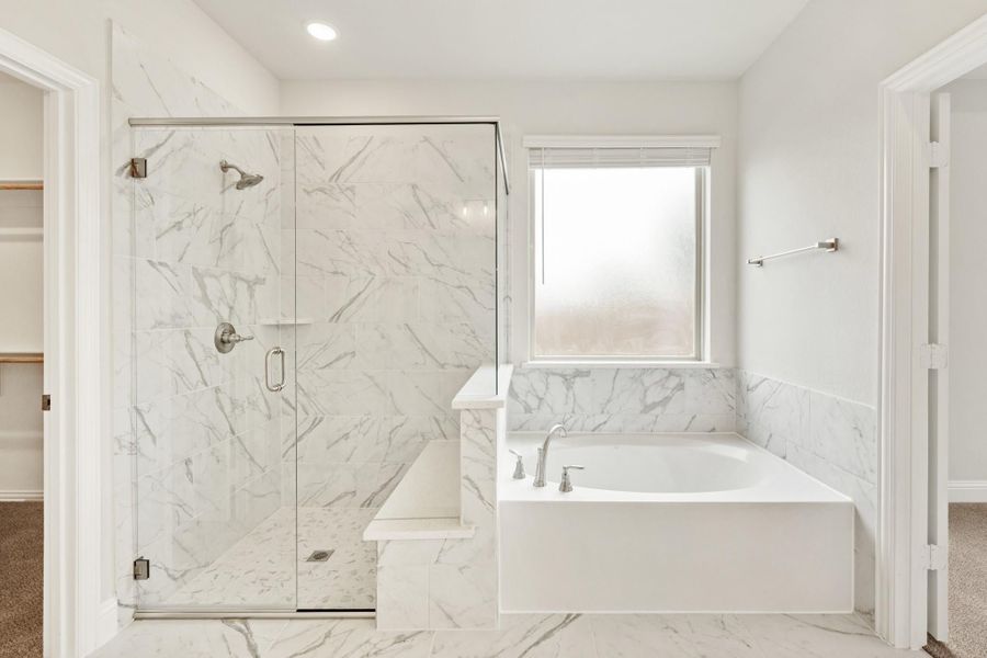 Master bathroom with marble tile walls, glass-enclosed shower with bench, and soaking tub