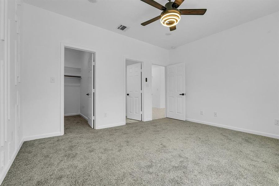 Unfurnished bedroom featuring a walk in closet, light colored carpet, a closet, and ceiling fan