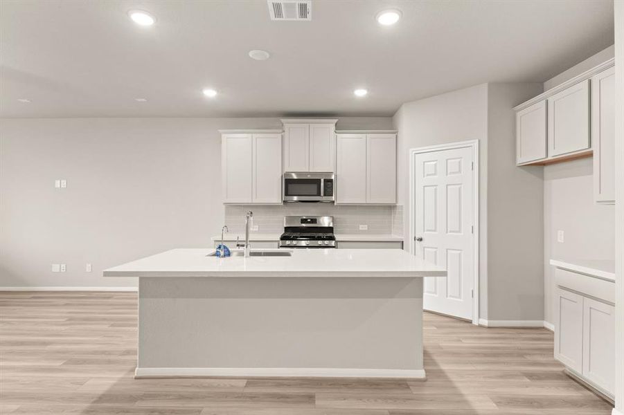 This light and bright kitchen features a large quartz island, white cabinets, a large sink overlooking your family room, recessed lighting, and beautiful backsplash.