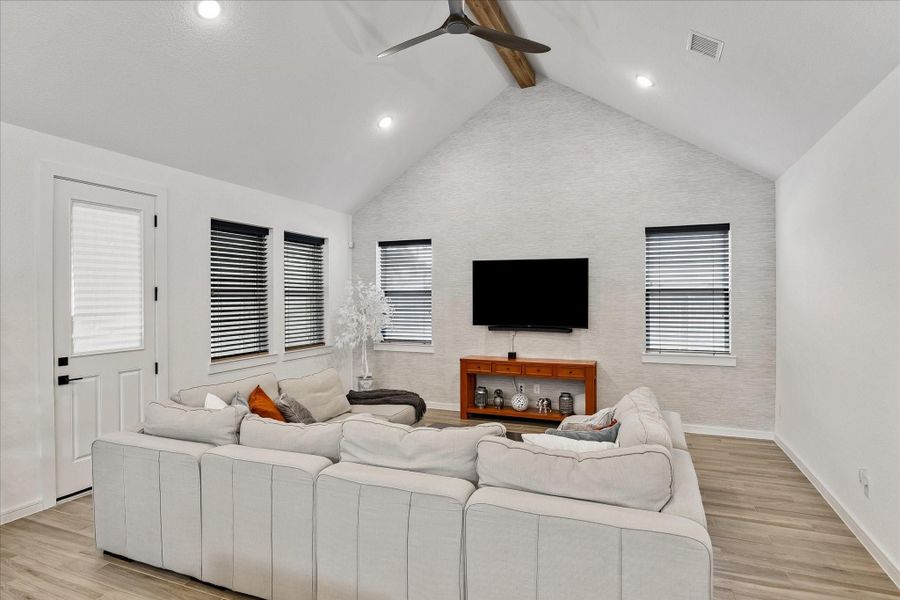 Dramatic vaulted living room anchored by a designer accent wall, exposed wood beam detail, and expansive ceiling height that creates an open, airy feel.