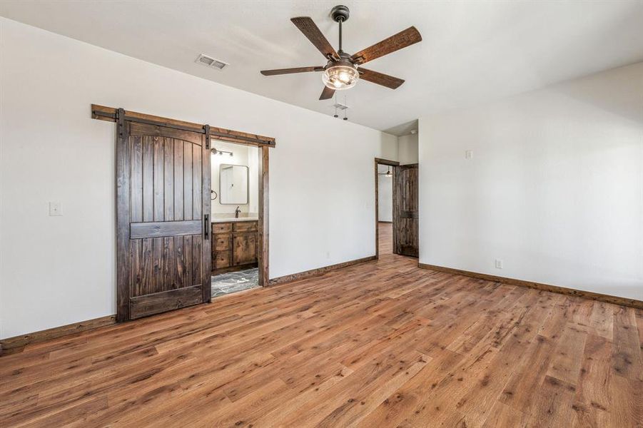 Unfurnished bedroom featuring baseboards, a barn door, visible vents, and wood-type flooring