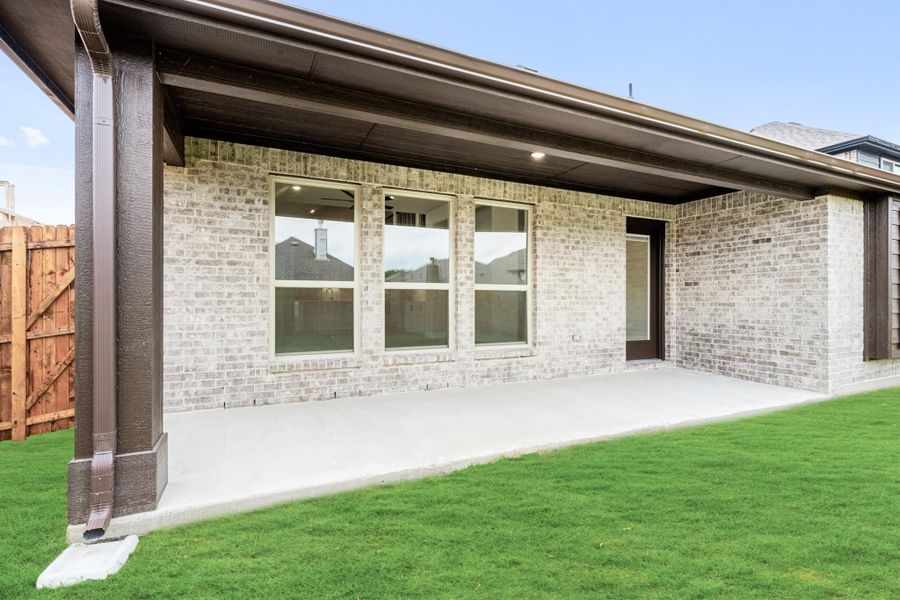 Covered back patio with concrete floor, brick exterior, large windows, and green lawn