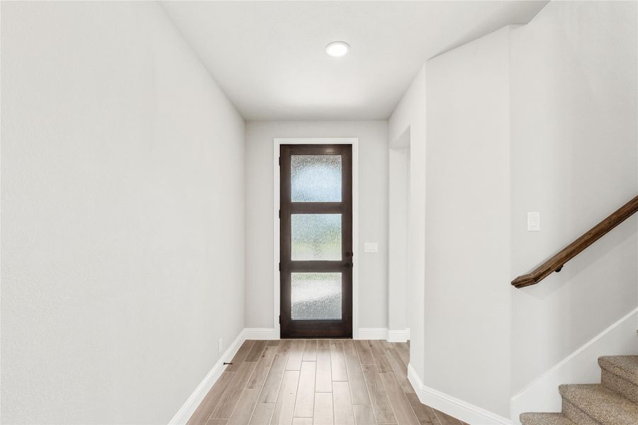 Entryway with dark wood front door with glass panels, light wood floors, and staircase with wood handrail