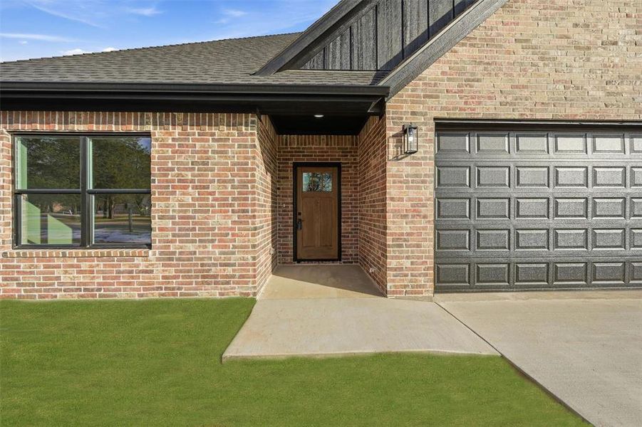 View of exterior entry with brick siding, concrete driveway, and roof with shingles View of exterior entry with brick siding, concrete driveway, and roof with shingles