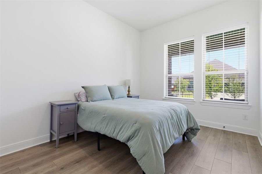 Spacious room featuring wood-finish flooring, two large windows with blinds, white trim, and white walls Spacious room featuring wood-finish flooring, two large windows with blinds, white trim, and white walls
