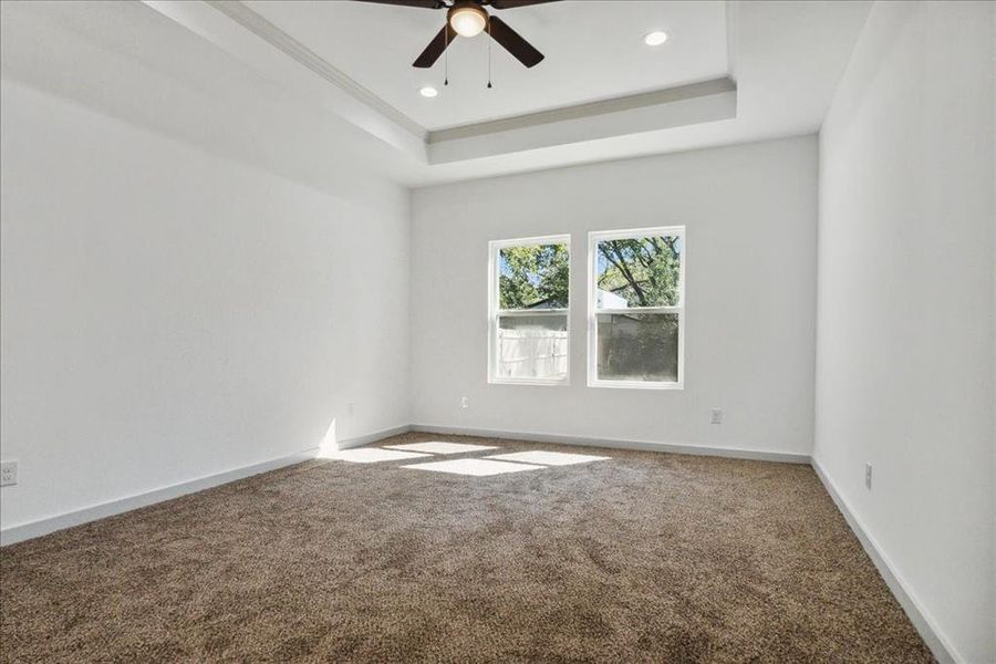 Carpeted empty room featuring ceiling fan and a tray ceiling