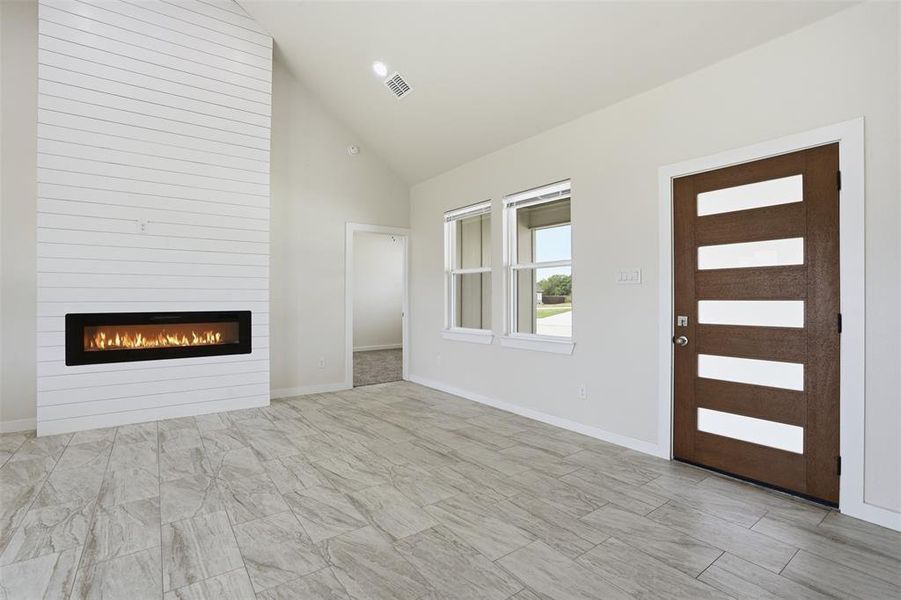 Living area featuring a floor-to-ceiling shiplap fireplace with a linear insert, vaulted ceiling, and wood-look tile flooring