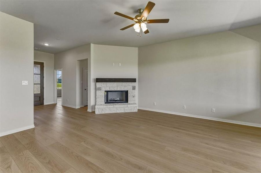Spacious living area featuring wood-finish flooring, a white brick fireplace with a dark wood mantel, and a ceiling fan with integrated lighting