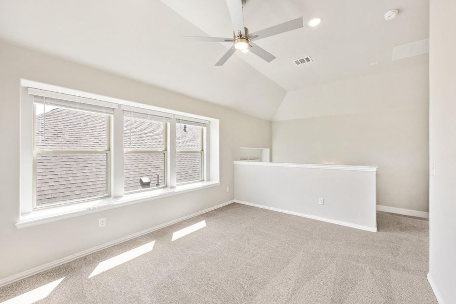 Empty bedroom with vaulted ceiling, ceiling fan, carpet flooring, and large triple window