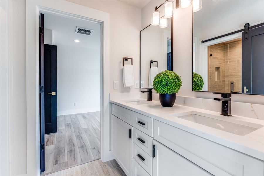 Bathroom featuring double vanity, light wood finished floors, and a tile shower