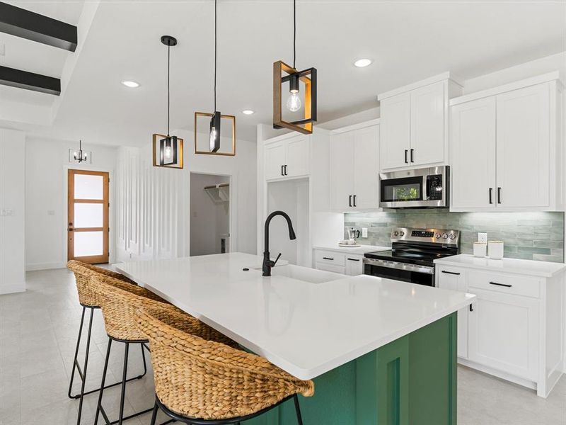 Kitchen featuring white cabinets, appliances with stainless steel finishes, backsplash, a center island with sink, and a breakfast bar