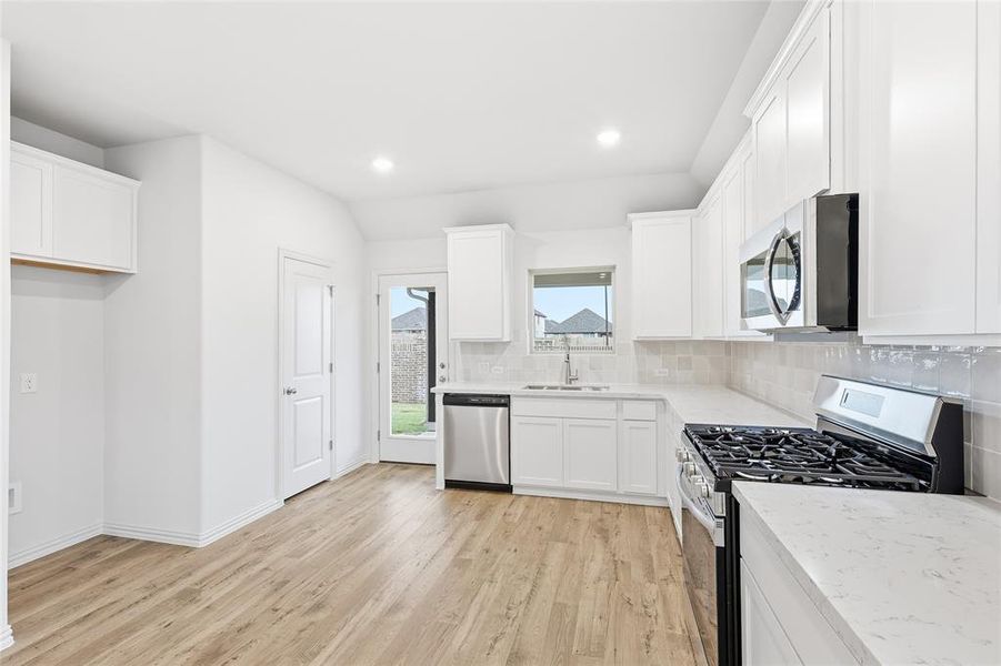 Kitchen with stainless steel appliances, white cabinets, light wood finished floors, backsplash, and light stone counters